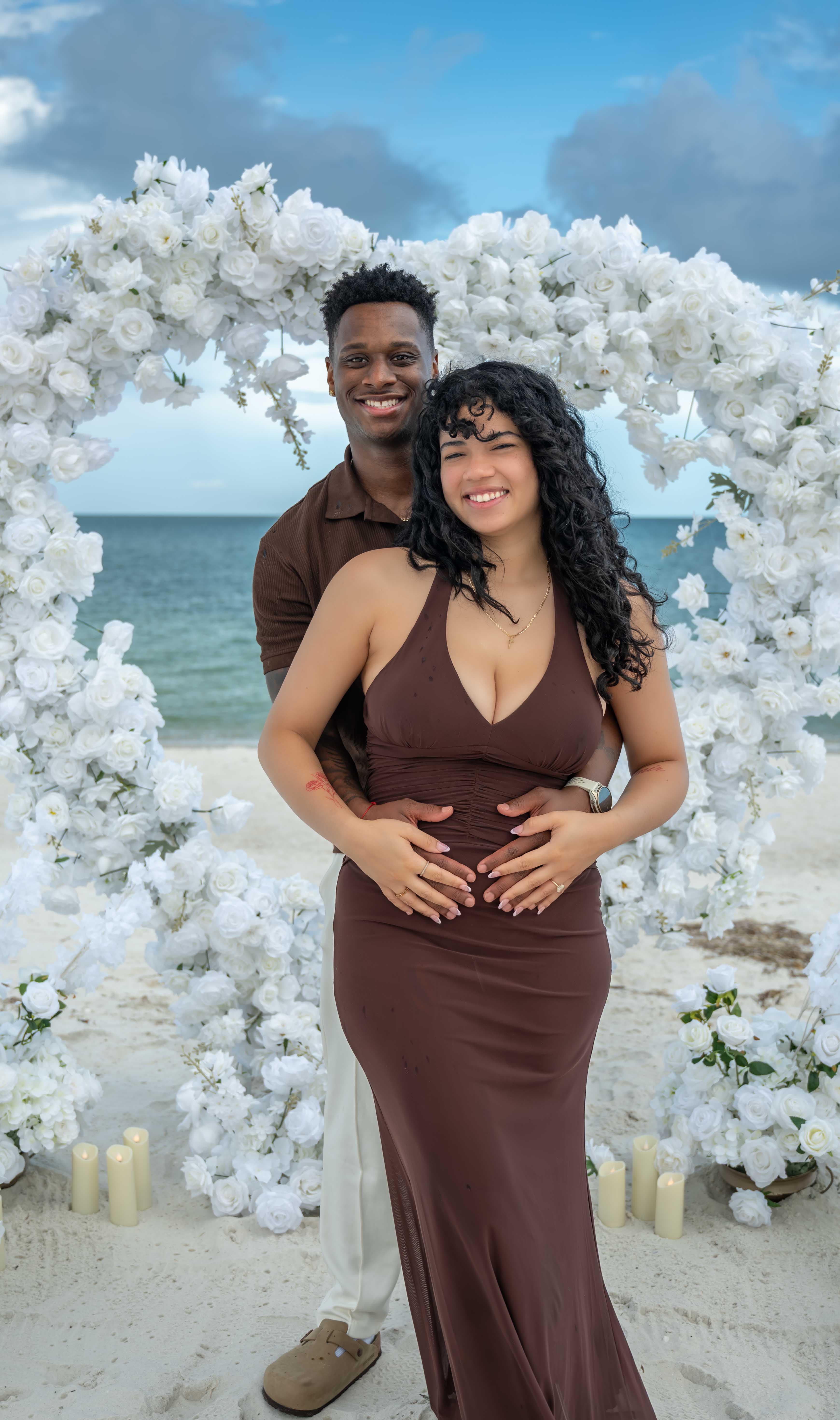 Couple embracing under a floral arch, beach engagement session