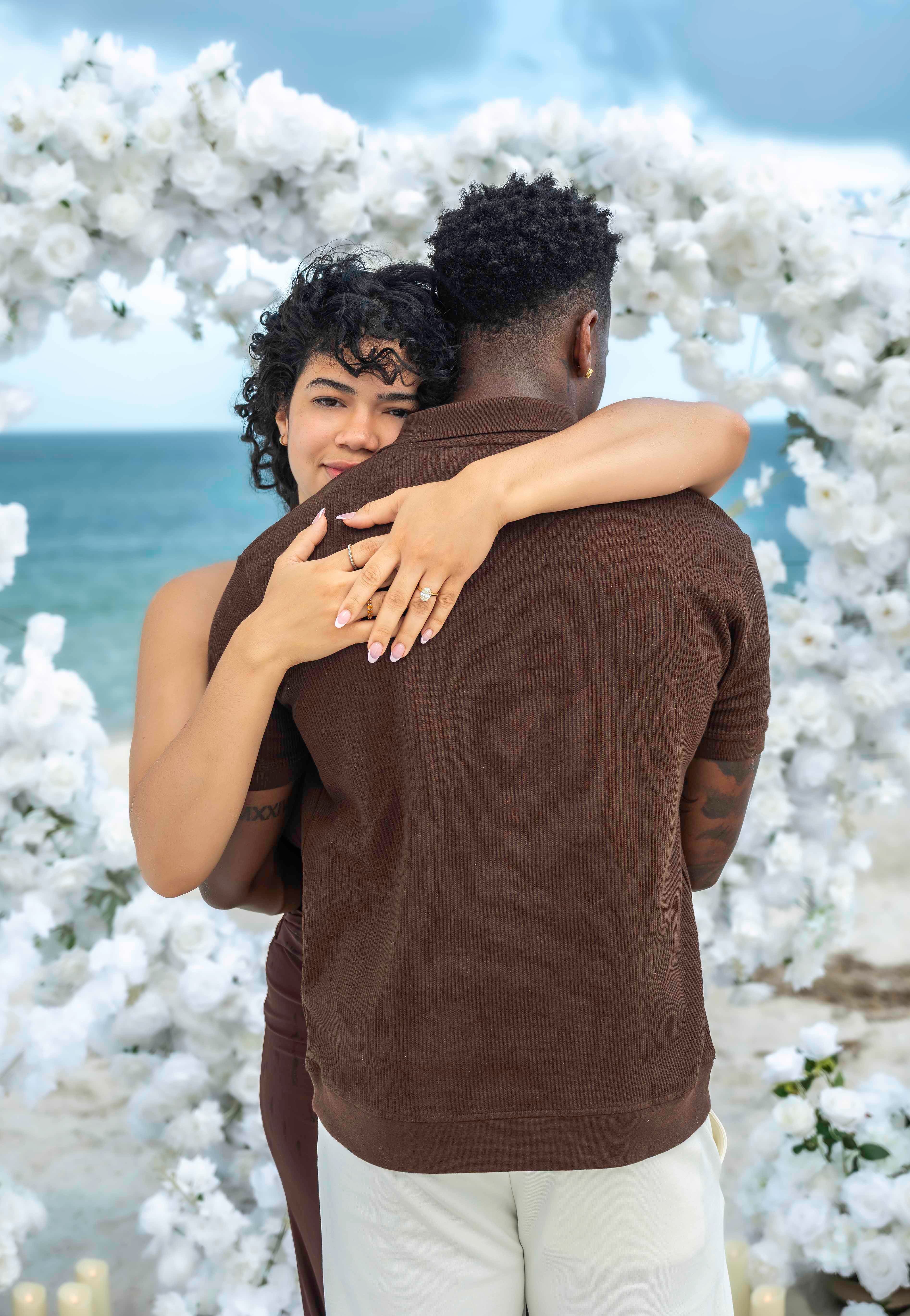 Couple embracing on the beach, engagement ring detail