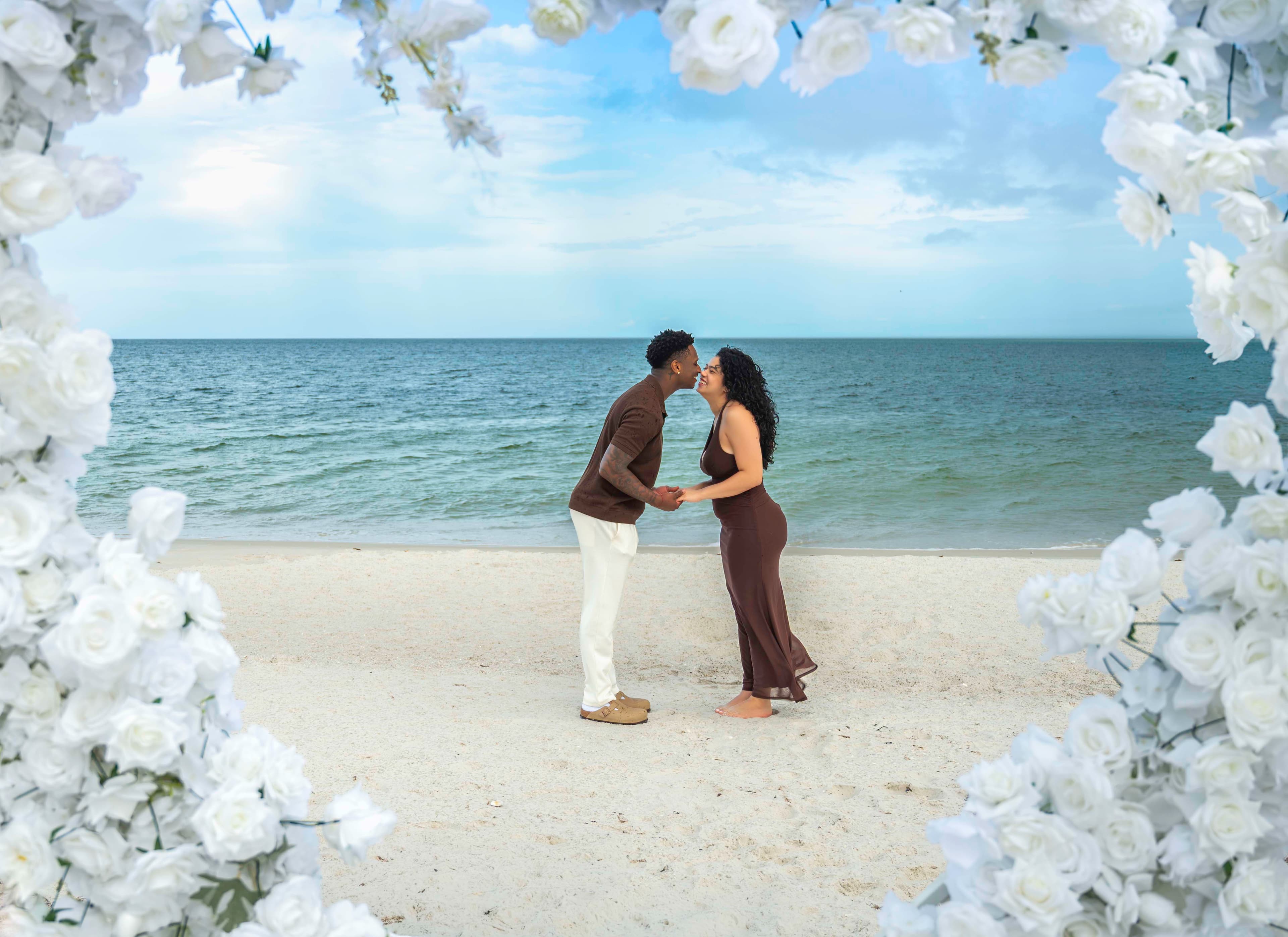 Couple sharing a kiss on the beach under a floral arch