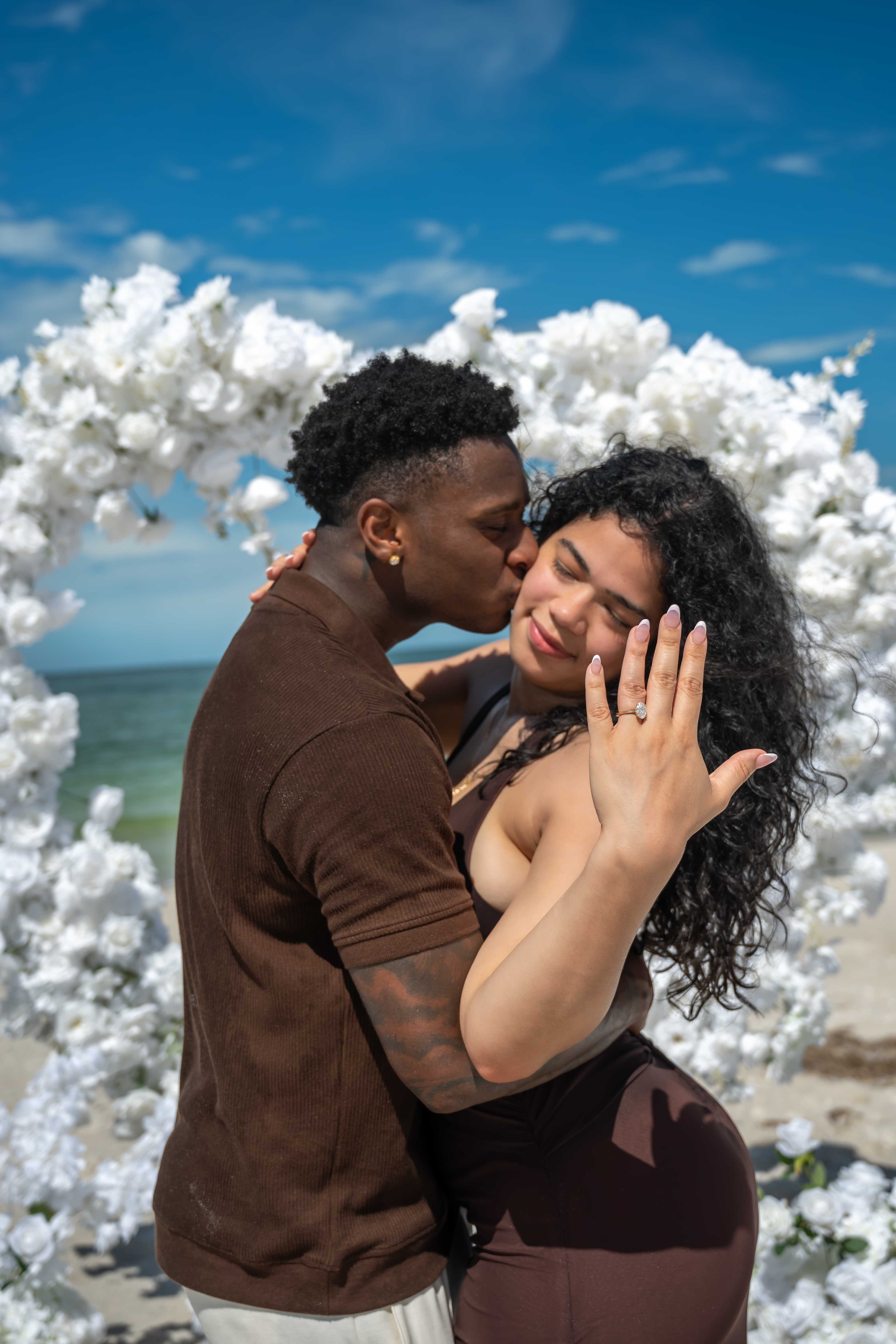 Couple embracing on a sunny beach under a floral arch