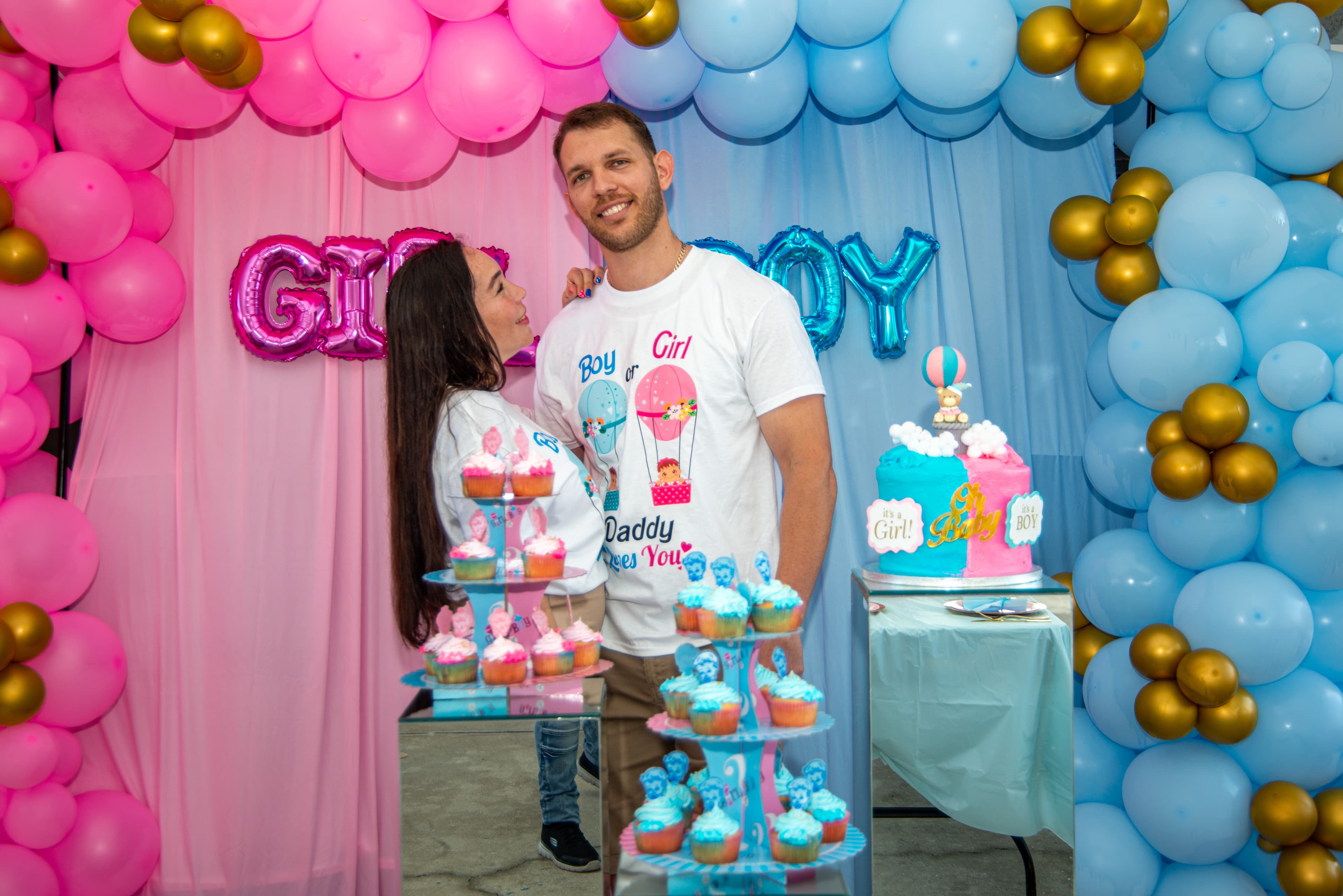 Gender reveal couple posing with custom t-shirts and dessert table