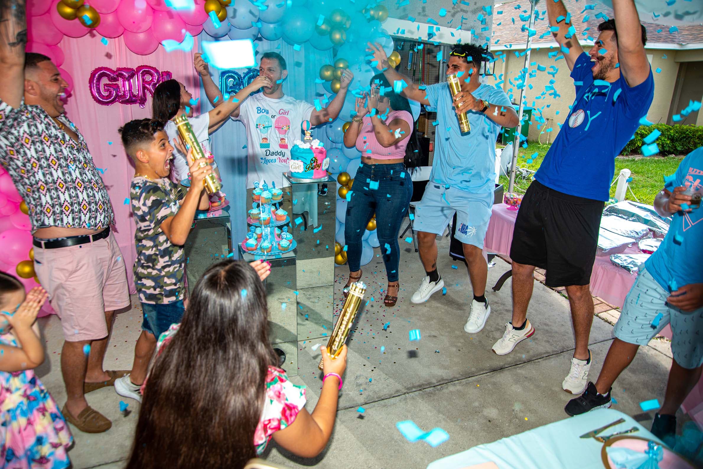 Guests cheering as blue confetti fills the air at a gender reveal party