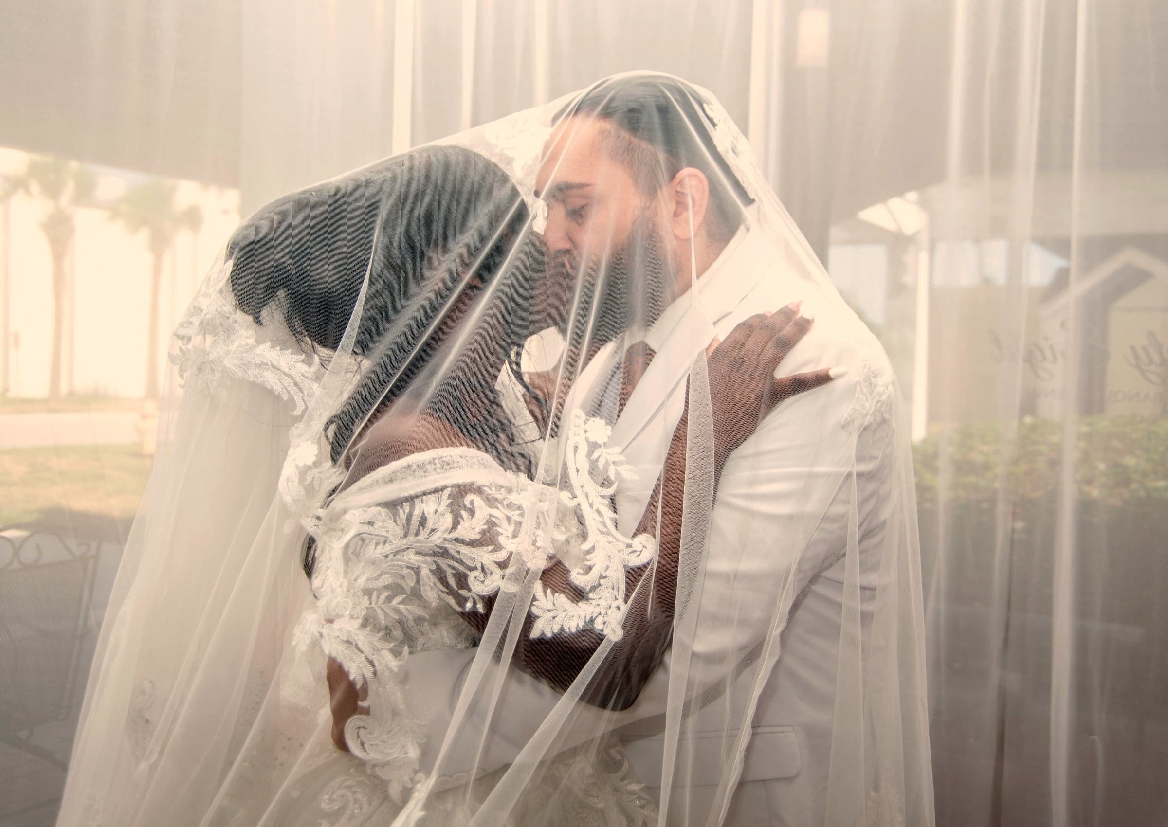 Bride and groom kiss under veil, dramatic wedding portrait