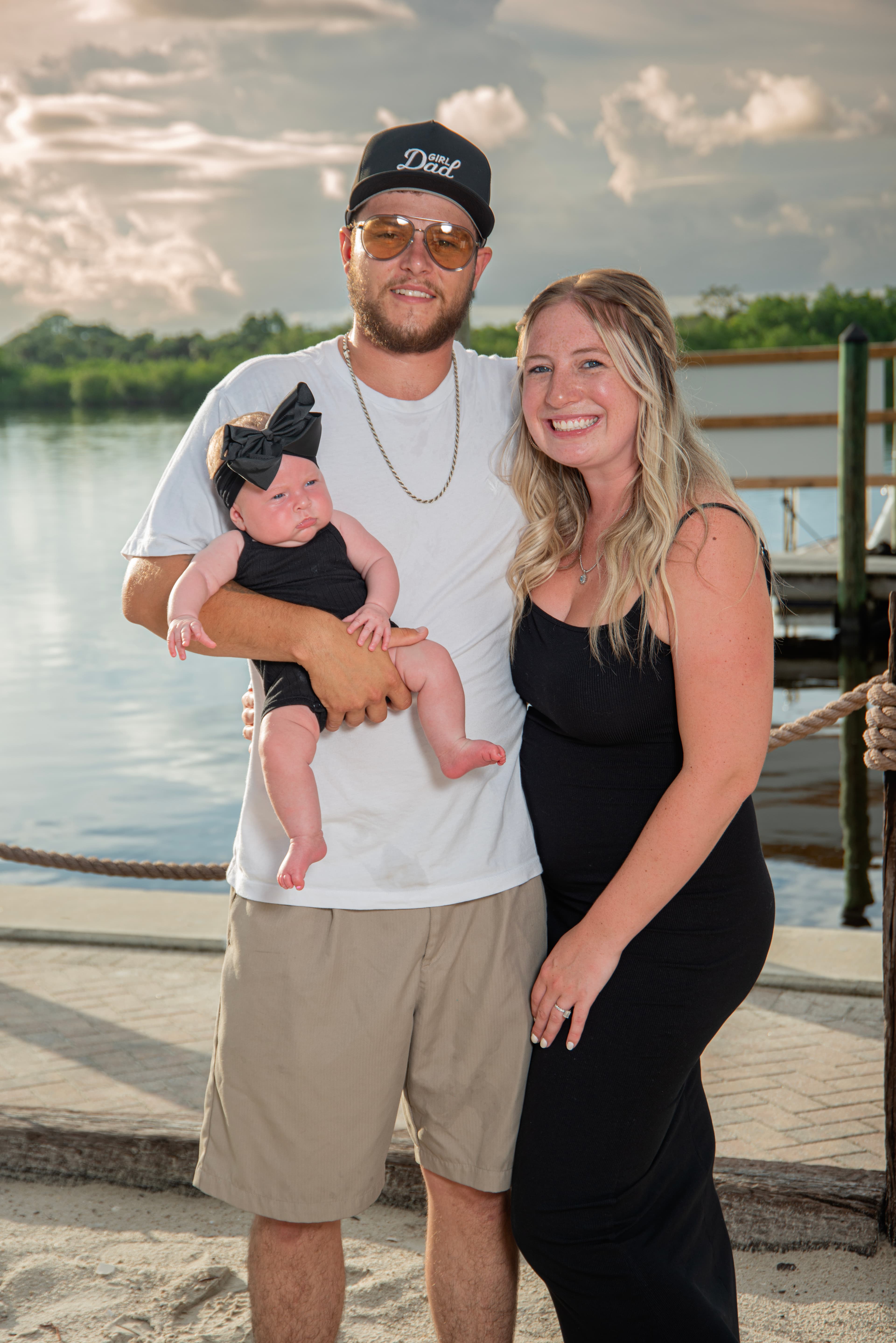 New parents holding their baby on the dock at sunset